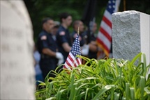 Closeup photo of gravestone with members of the military in background 