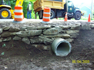 Opening of large drainage pipe surrounded by large stones - located under road level