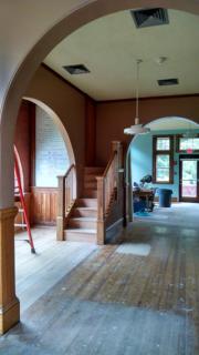 Interior picture showing work being done.  In process hardwood floor restoration, new stair case, and a pretty archway